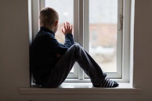 51612315 - young boy sitting on a windowsill inside a house waving to someone outside, view from the side