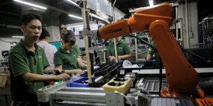 In this Aug. 21, 2015 photo, a Chinese man works amid orange robot arms at Rapoo Technology factory in southern Chinese industrial boomtown of Shenzhen. Factories in China are rapidly replacing those workers with automation, a pivot that’s encouraged by rising wages and new official directives aimed at helping the country move away from low-cost manufacturing as the supply of young, pliant workers shrinks. (AP Photo/Vincent Yu)